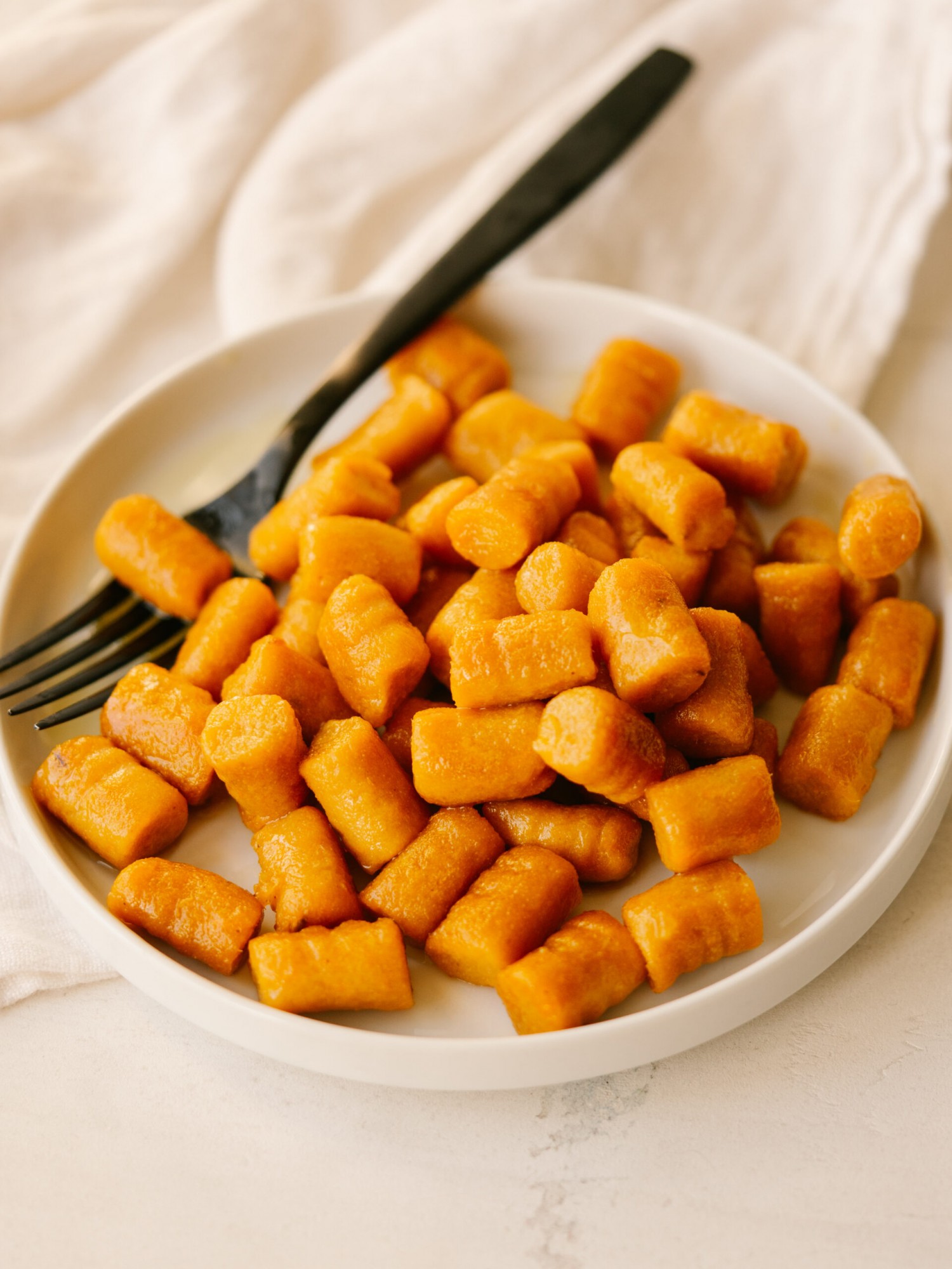 Three quarter view of sweet potato gnocchi on a white plate with a black fork