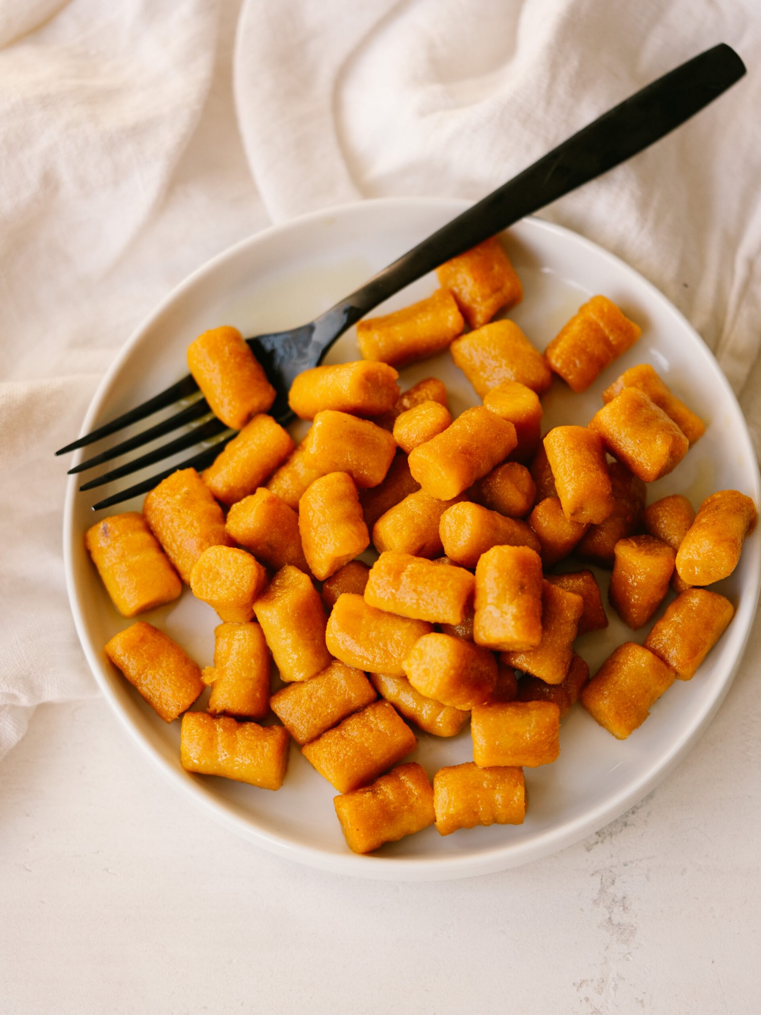 Above view of sweet potato gnocchi on a white plate with a black fork on it