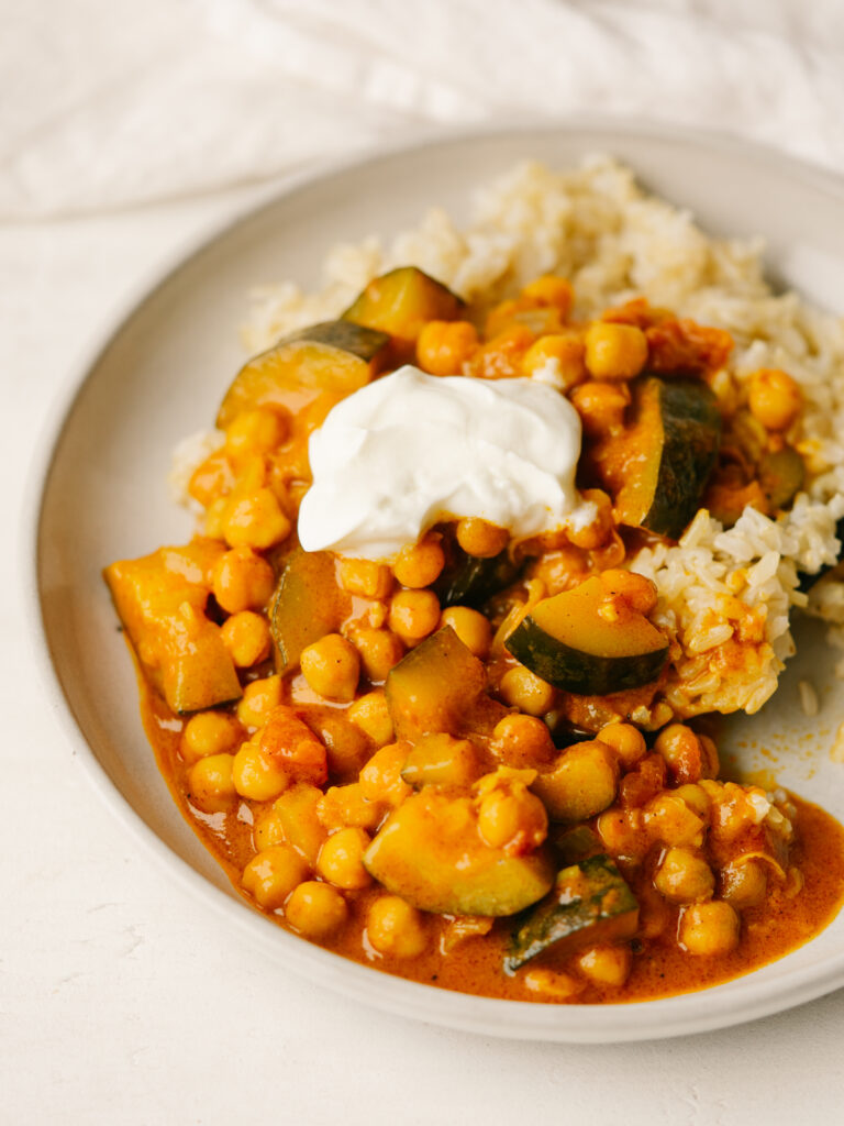 Creamy chickpea and vegetable stew on a plate with brown rice and a dollop of sour cream