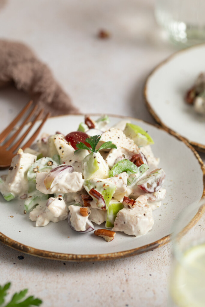 a three quarter view of chicken waldorf salad on a white plate with a fork next to it