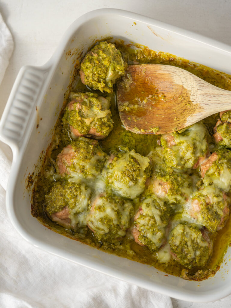 Above view of a wooden spoon in a casserole dish of pesto meatballs