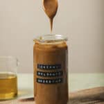 creamy balsamic vinaigrette in a mason jar with a spoon above the opening of the jar on a wooden cutting board