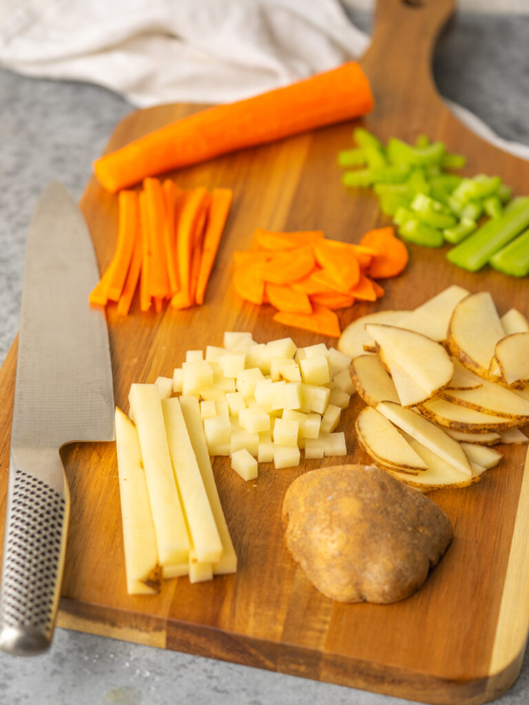 Three quarter view of different vegetables demonstrating knife cuts on a cutting board