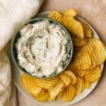 easy spinach dip in a green bowl on a plate with chips on the plate
