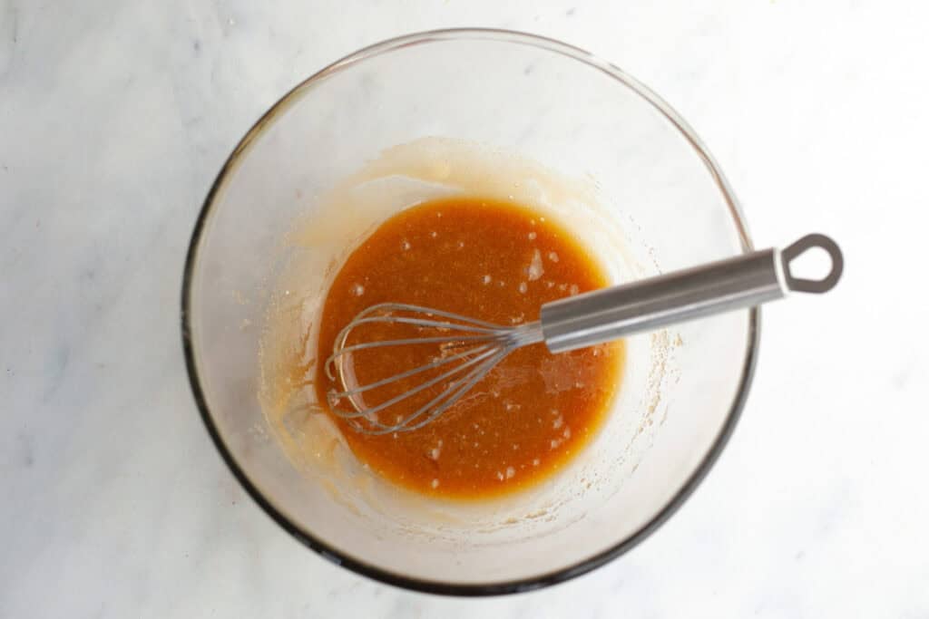 sugar, oil, and egg combined in a glass bowl with a whisk in it
