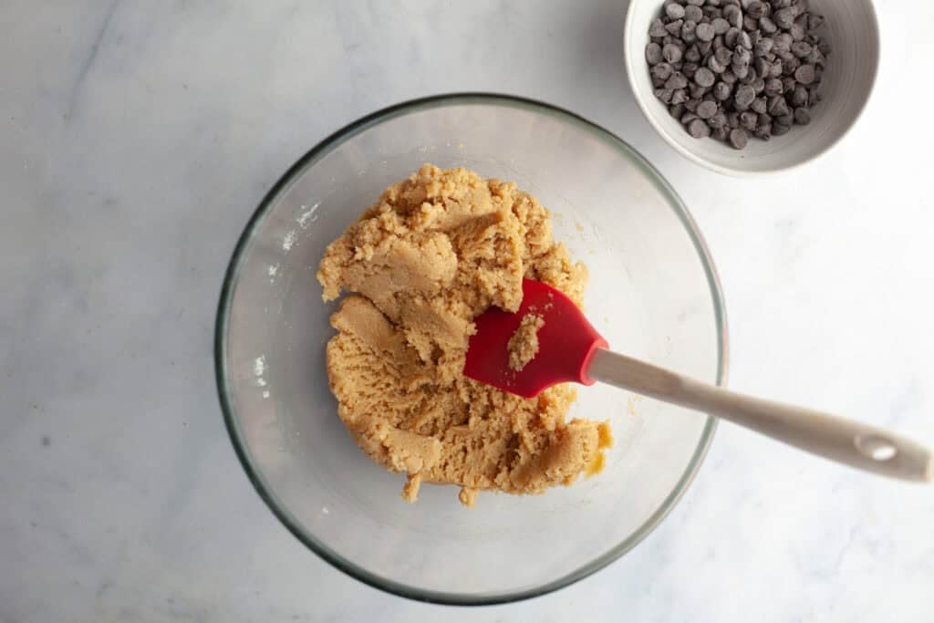 chocolate chip cookie dough in a glass bowl with a spatula in it