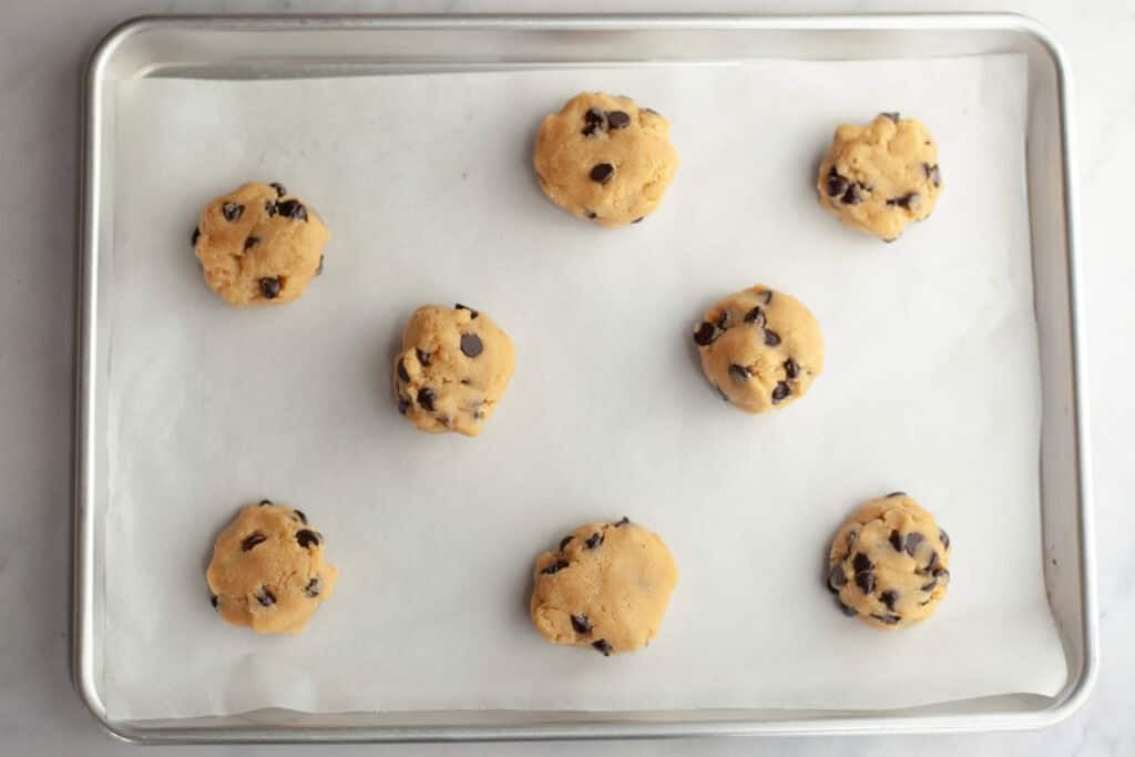 cookie dough balls on a baking sheet with parchment paper on it