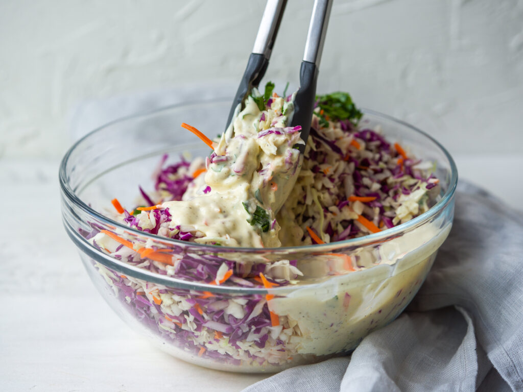 side view of cabbage being tossed in coleslaw dressing in a bowl