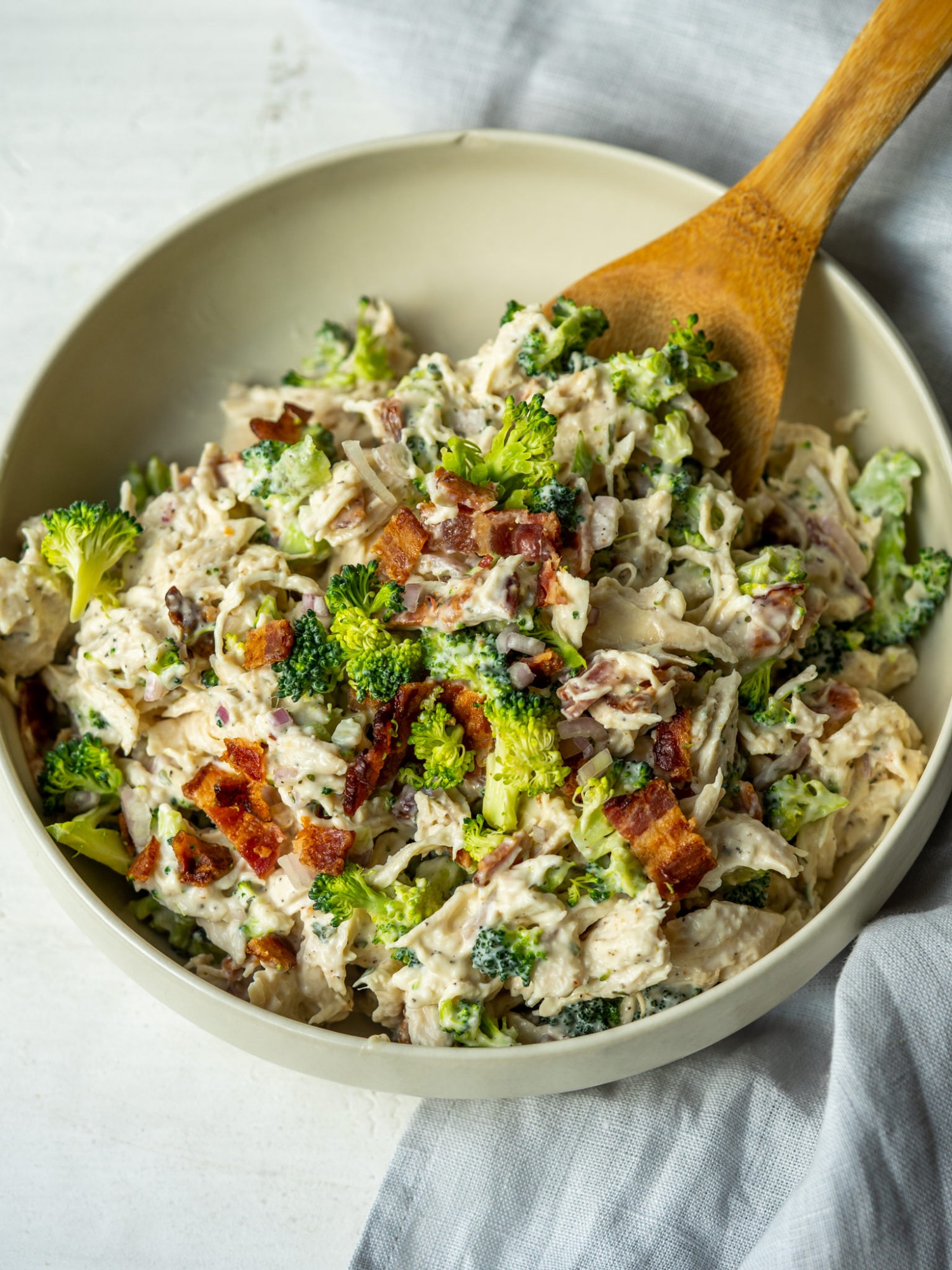 an above view photo of bacon ranch chicken salad in a bowl with a wooden spoon in it