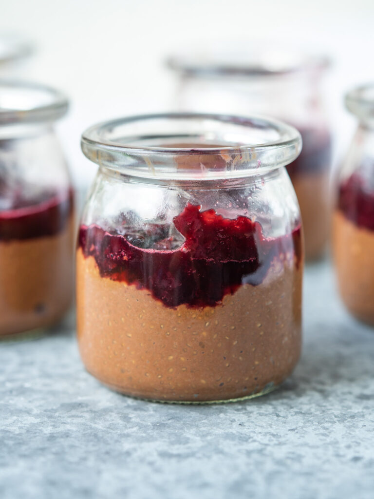 Side view of a jar of chocolate chia seed pudding with cherry compote on top