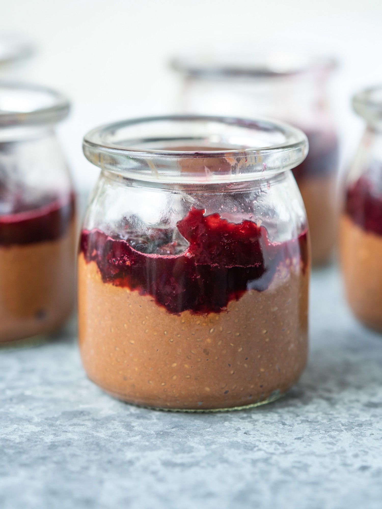 Side view of chocolate chia pudding in a glass jar with cherry compote on top