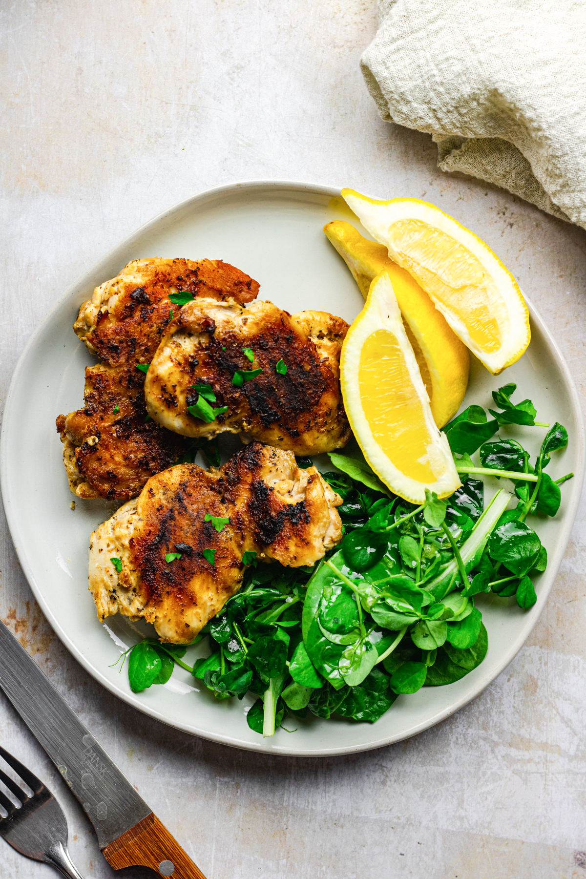 Grilled chicken thighs on a plate served with lemon and greens