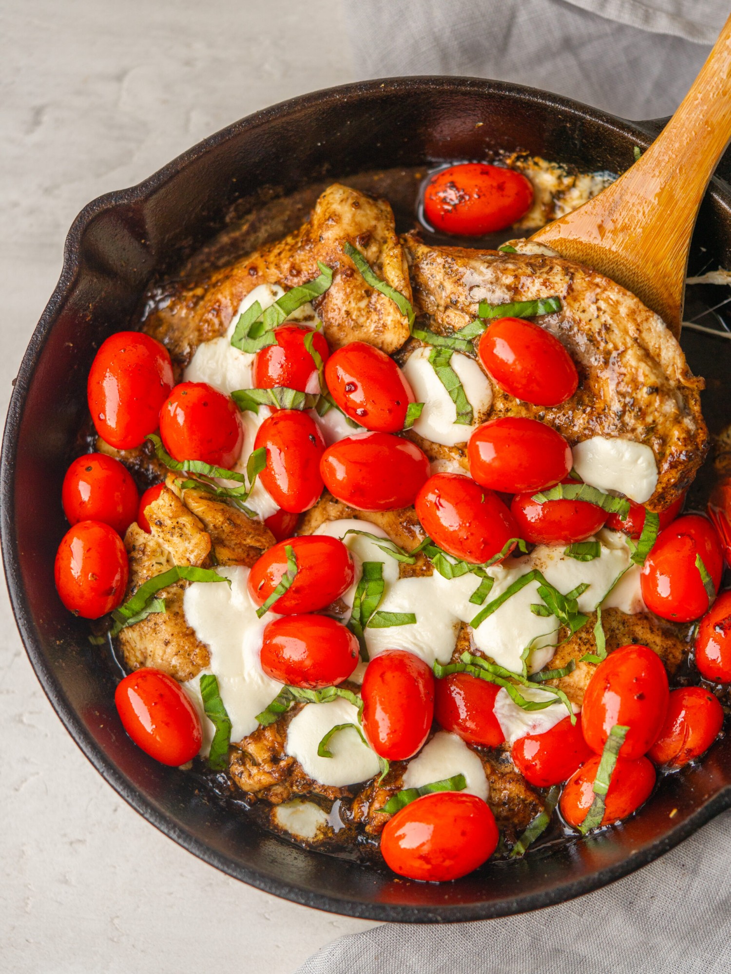 Above view of chicken caprese skillet in a cast iron with a wooden spoon