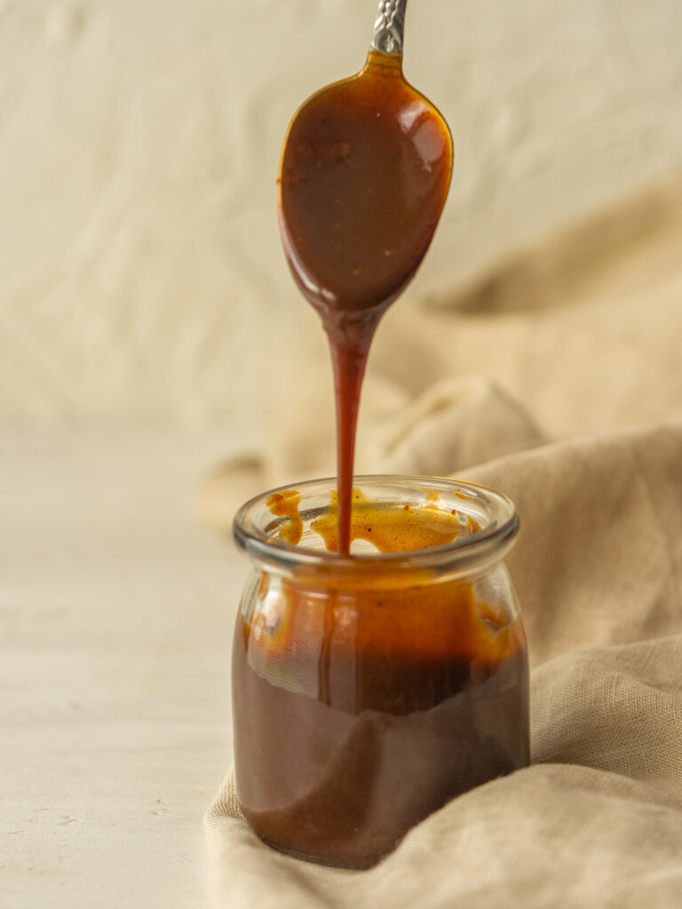Side view of pumpkin spice syrup dripping off a spoon into a glass jar