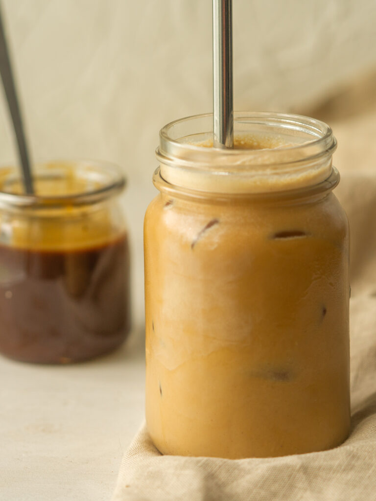 Side view of an iced pumpkin spice latte next to a jar of pumpkin spice syrup