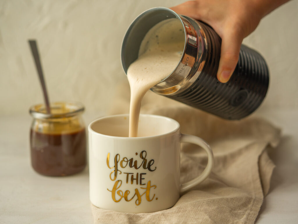 Side view of a starbucks pumpkin spice latte foam pouring into a mug with a jar of pumpkin syrup for coffee next to the mug