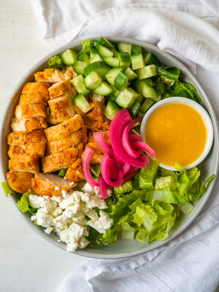 Colorful salad topped with sriracha chicken and pickled red onions