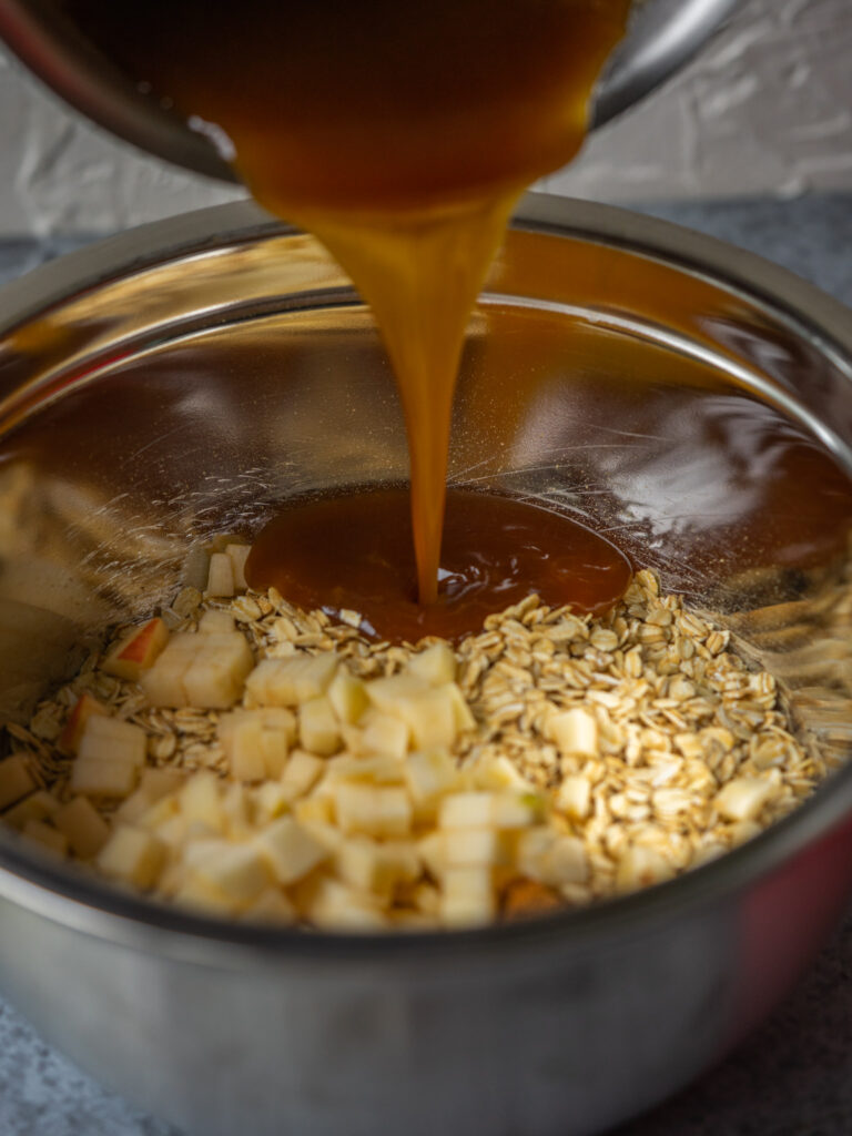 a close up of caramel drizzling into a bowl with granola and apple in it