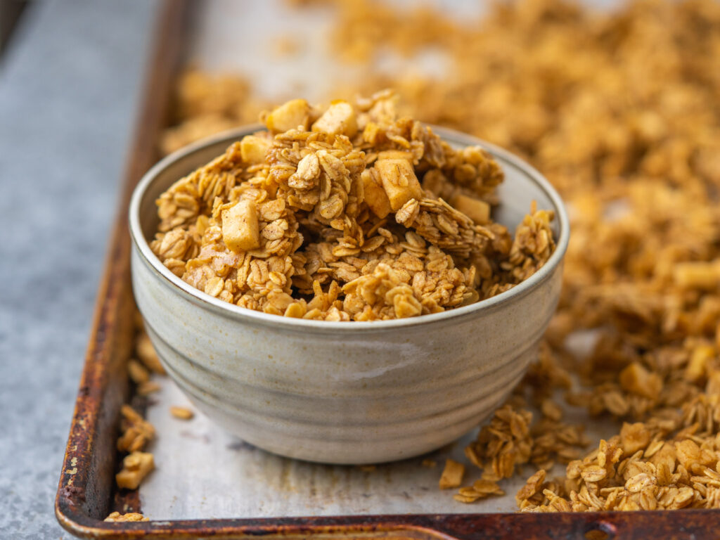a photo of a bowl of salted caramel apple granola on a baking sheet