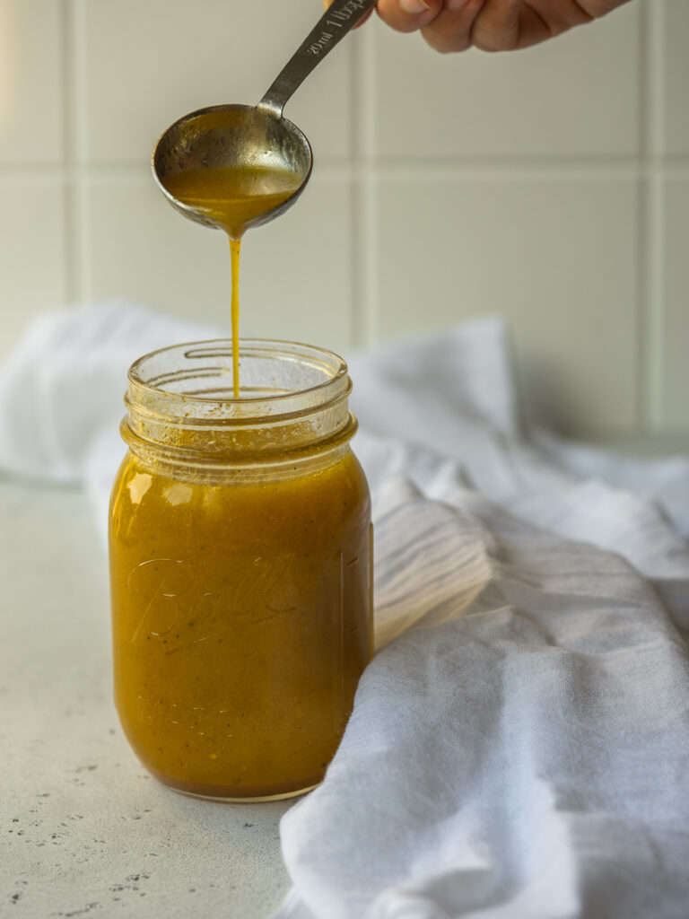 Side view of a spoonful of dressing pouring into a mason jar