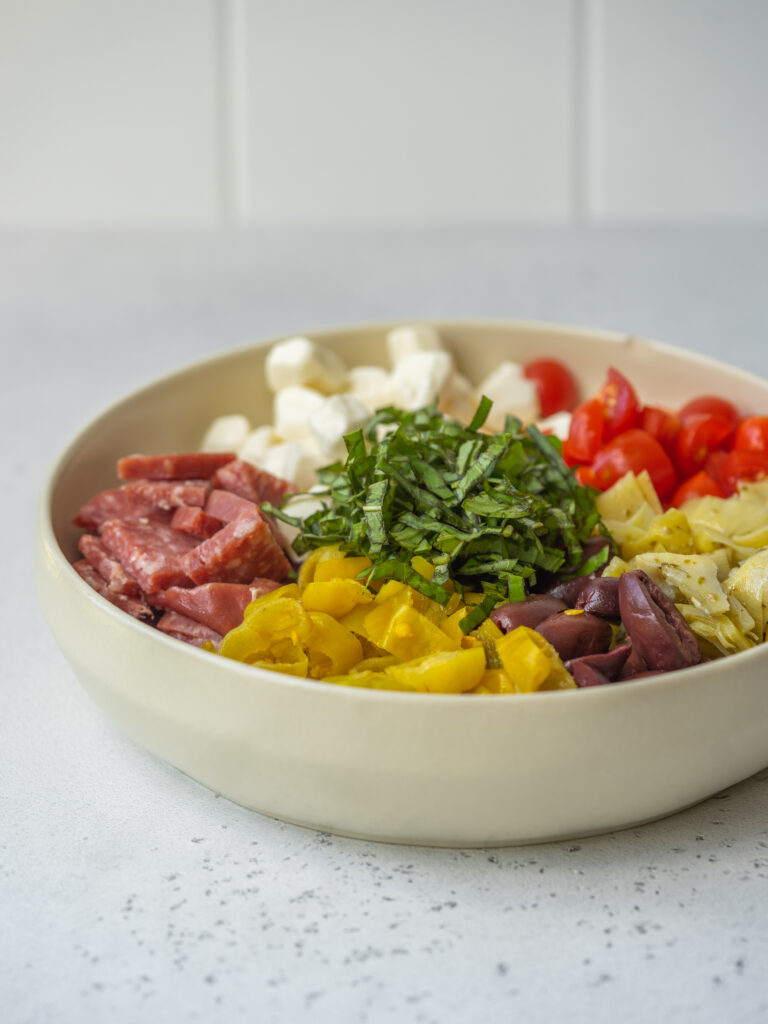 Three quarter view of ingredients for an antipasto salad recipe in a serving bowl