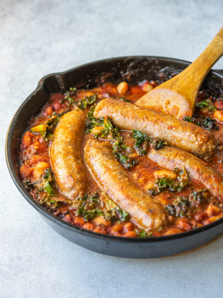 a three quarter view photo of the sausage skillet in a cast iron with a wooden spoon in it