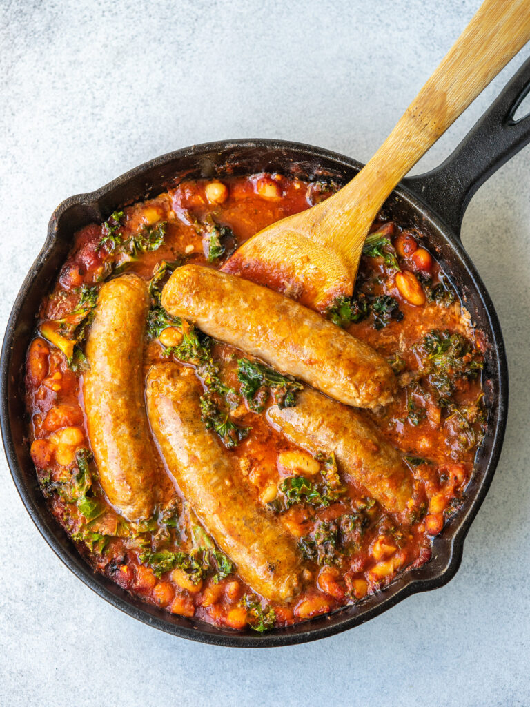 an above view image of sausage white bean and kale skillet with a wooden spoon in it