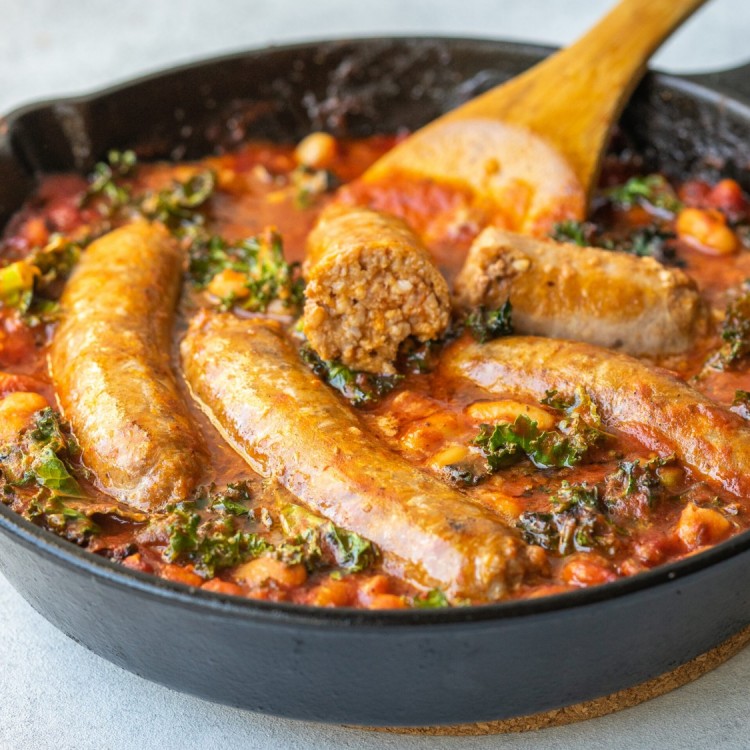 Three quarter view of sausage, kale, white beans, and tomato sauce in a cast iron skillet