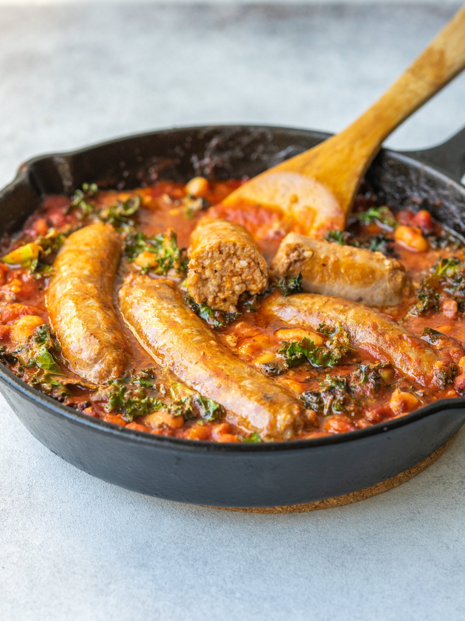 Three quarter view of sausage, kale, white beans, and tomato sauce in a cast iron skillet