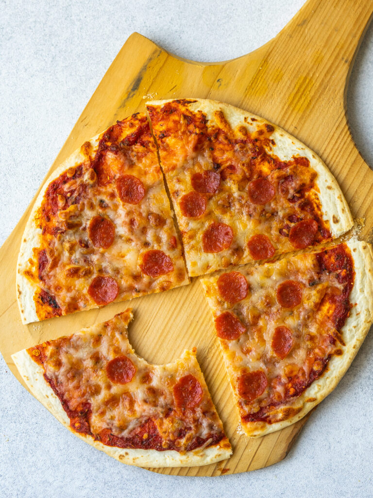 Above view of homemade pizza cut into four slices with a bite out of one slice