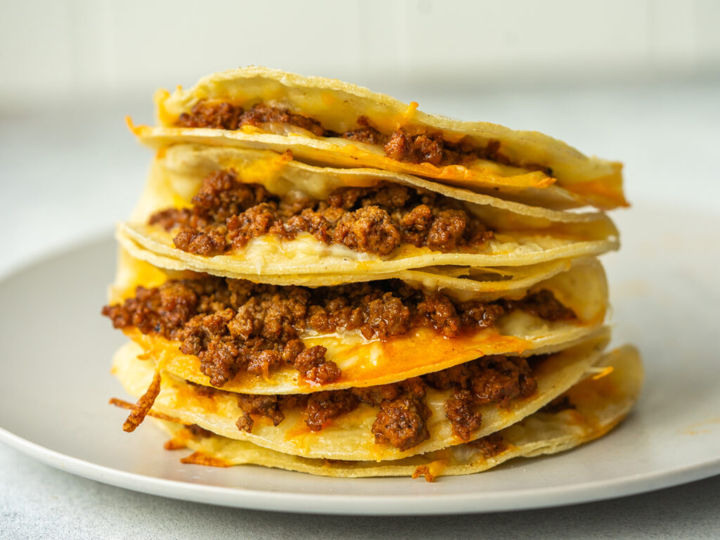Oven baked tacos stacked up on top of each other so you can see cheese and ground beef inside