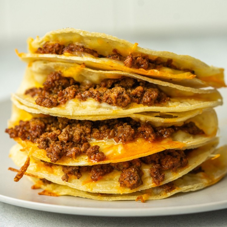 Side view of baked tacos stacked one on top of each other and you can see the cheese and seasoned ground beef inside each taco