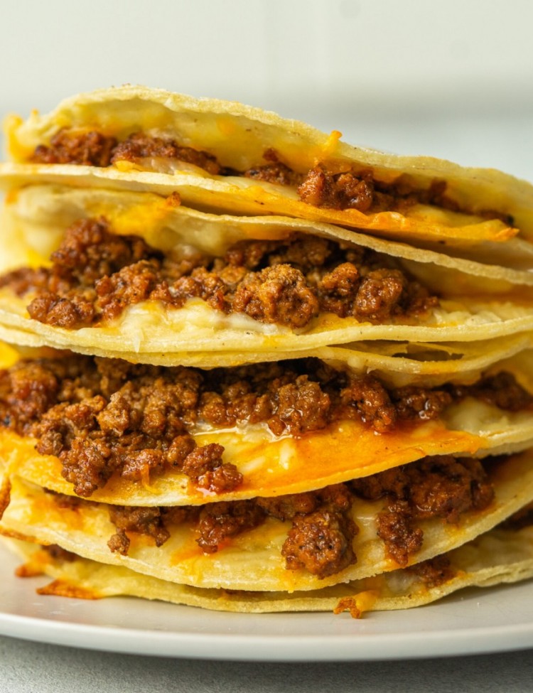 Side view of baked tacos stacked one on top of each other and you can see the cheese and seasoned ground beef inside each taco