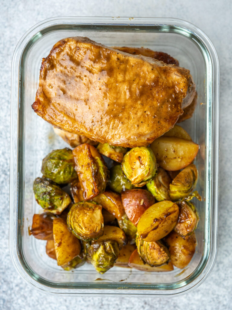 Above view of balsamic pork chop dinner with brussels sprouts and potatoes in a glass storage container