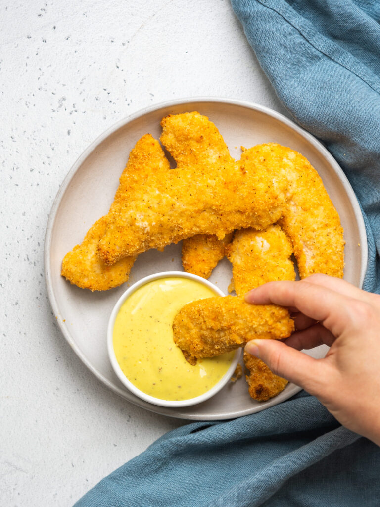 Above view of a baked breaded chicken tender dipping into a honey mustard sauce