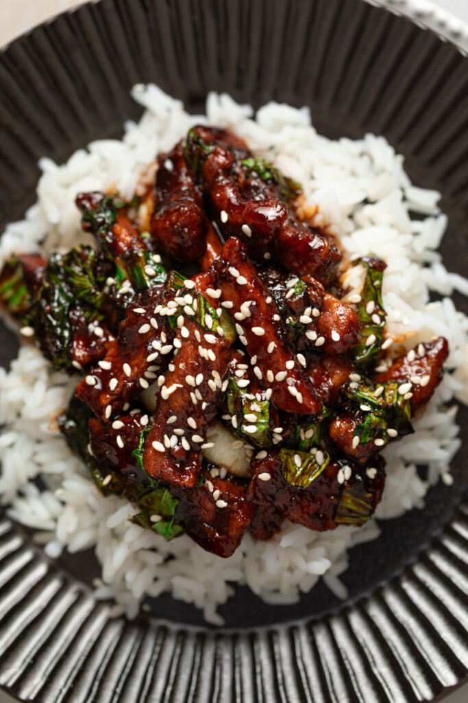 an above view image of terikyaki pork chops over white rice in a black bowl