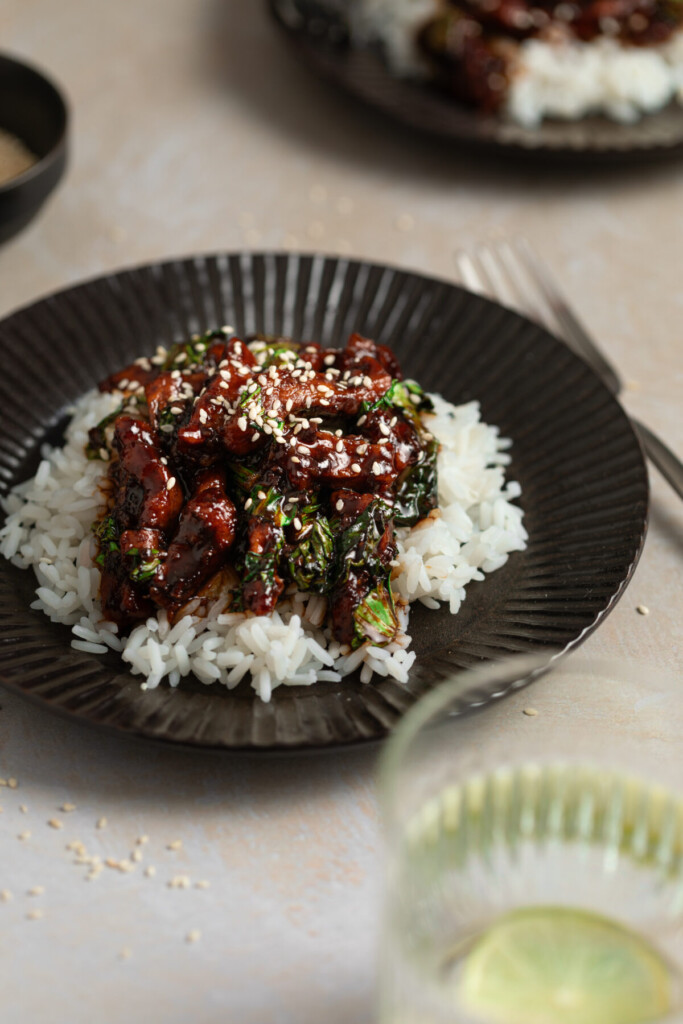 a three quarter photo of teriyaki beef over rice in a black bowl
