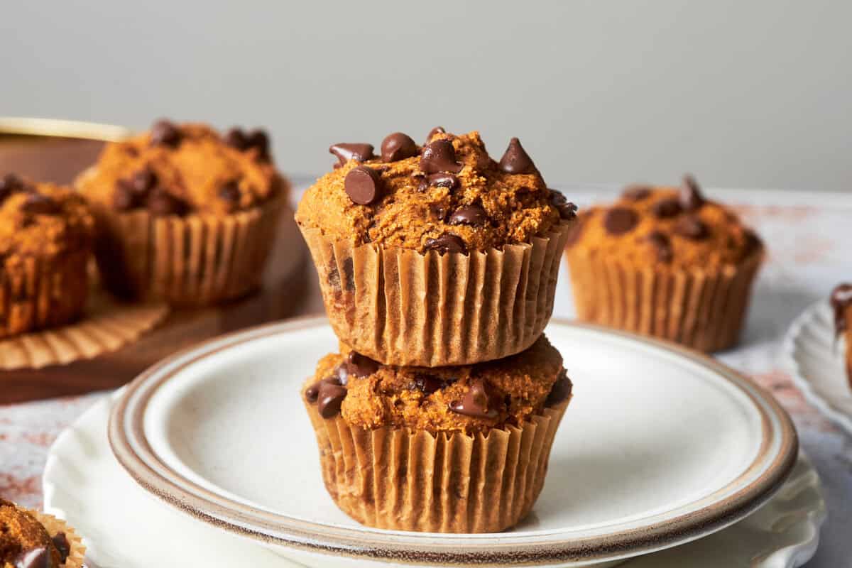 two pumpkin chocolate chip muffins stacked on a plate with a few in the background