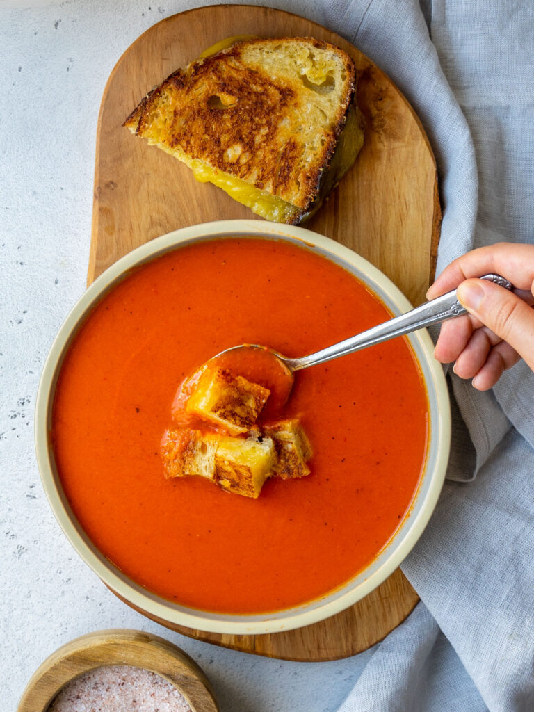 spoon dipping into a bowl of roasted red pepper and tomato soup