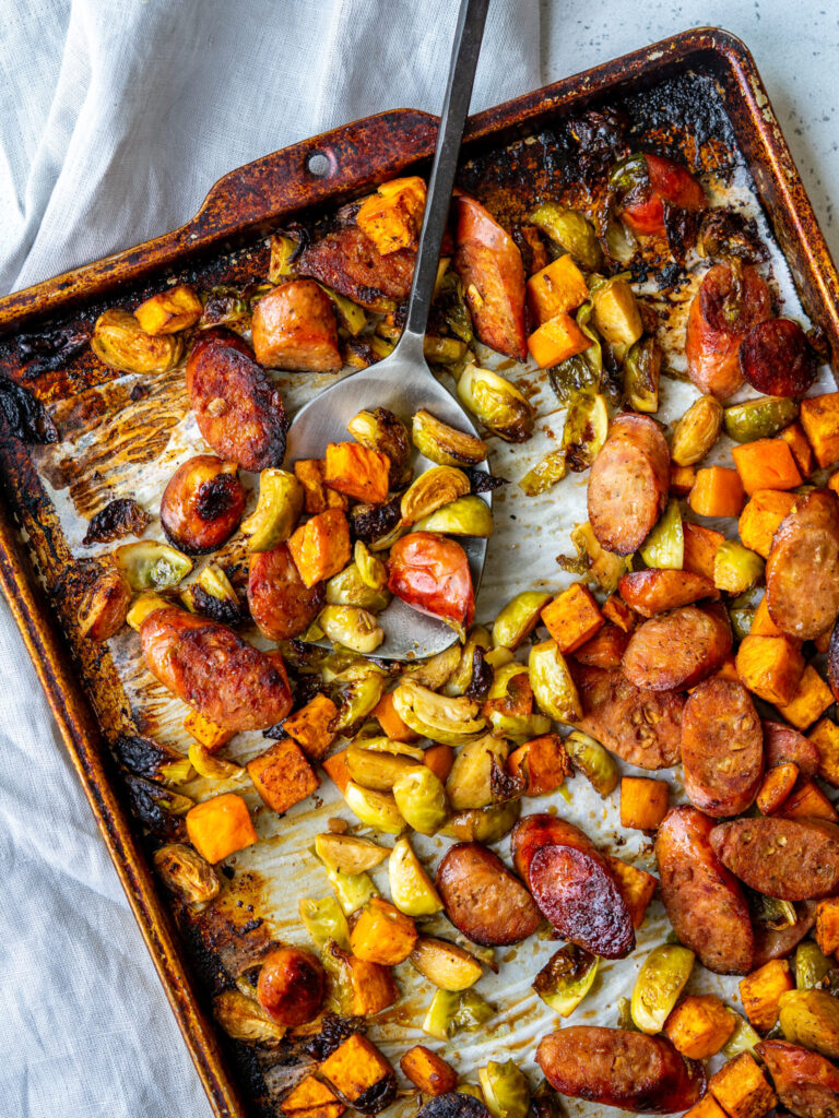 spoon scooping sheet pan supper made with chicken apple sausage, sweet potatoes, and brussels sprouts