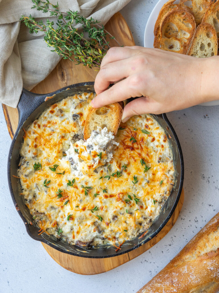 hand with toast dipping into stuffed mushroom dip