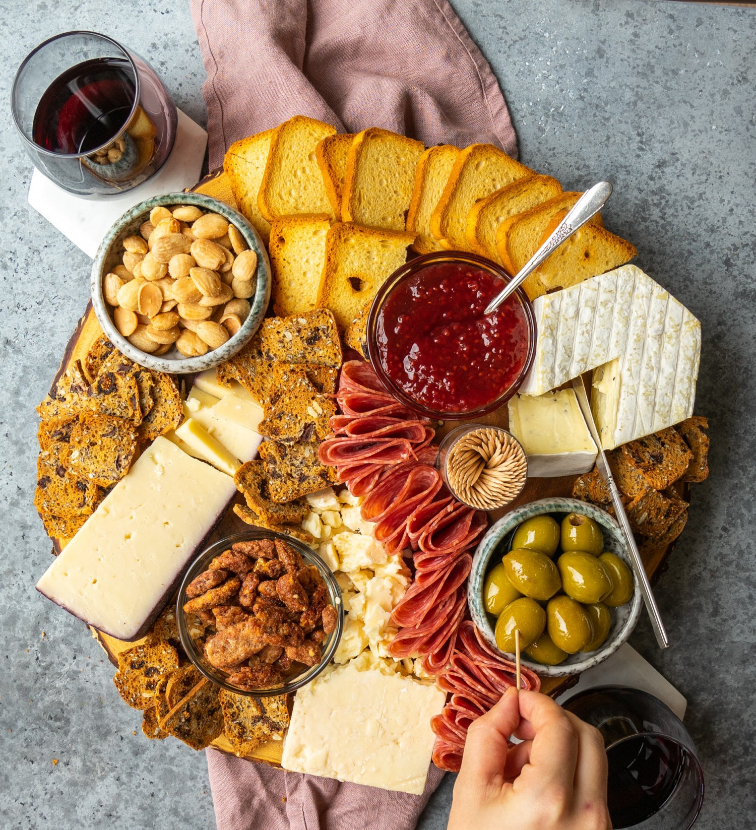 Above view of Trader Joe's holiday cheese board with a hand grabbing an olive