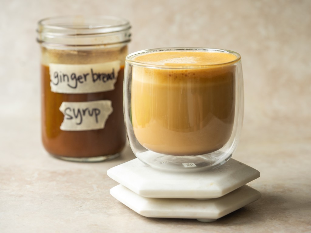 Gingerbread latte in a mug next to a jar of gingerbread syrup