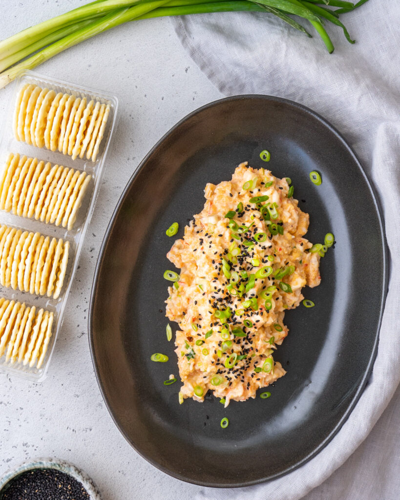 shrimp dip on a black platter with a pack of crackers