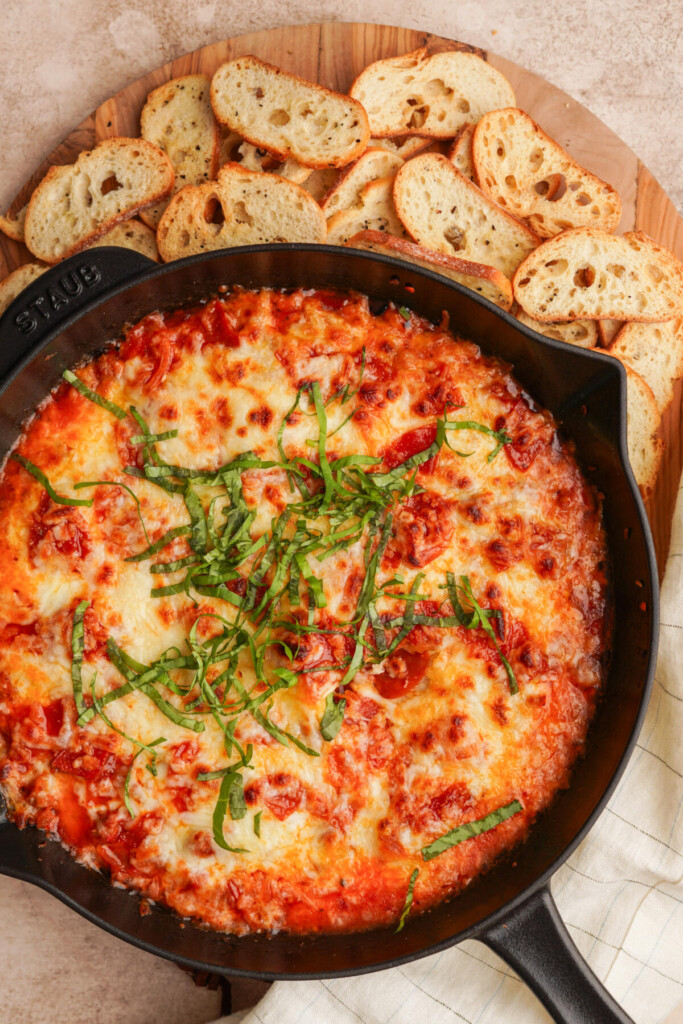 an above view photo of the pizza dip in a cast iron skillet with crostinis surrounding the side of the pan