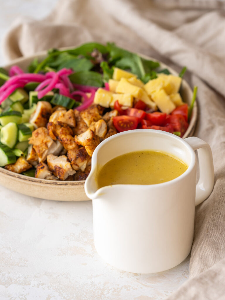 three quarter view of apple cider vinegar salad dressing in a small pitcher in front of a salad