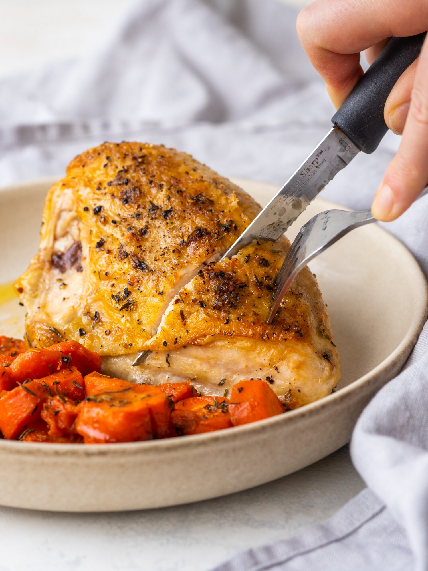 a photo of hands cutting the baked chicken breasts on a plate with carrots on it