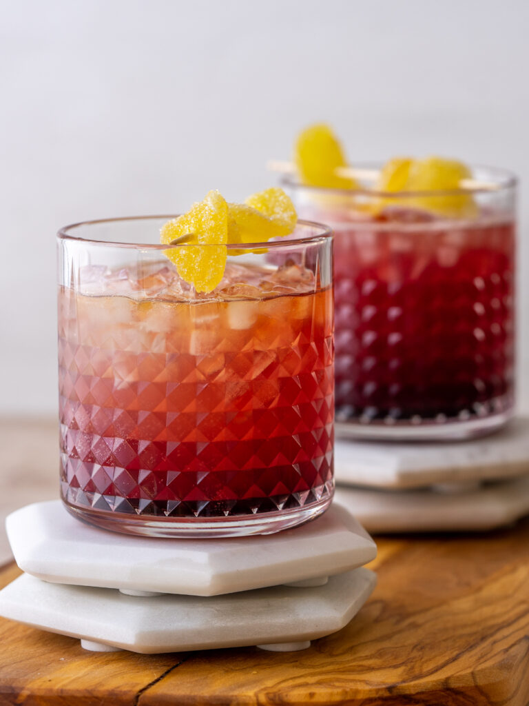 side view of cranberry Kentucky mule drinks in whisky glasses with a cadied ginger garnish