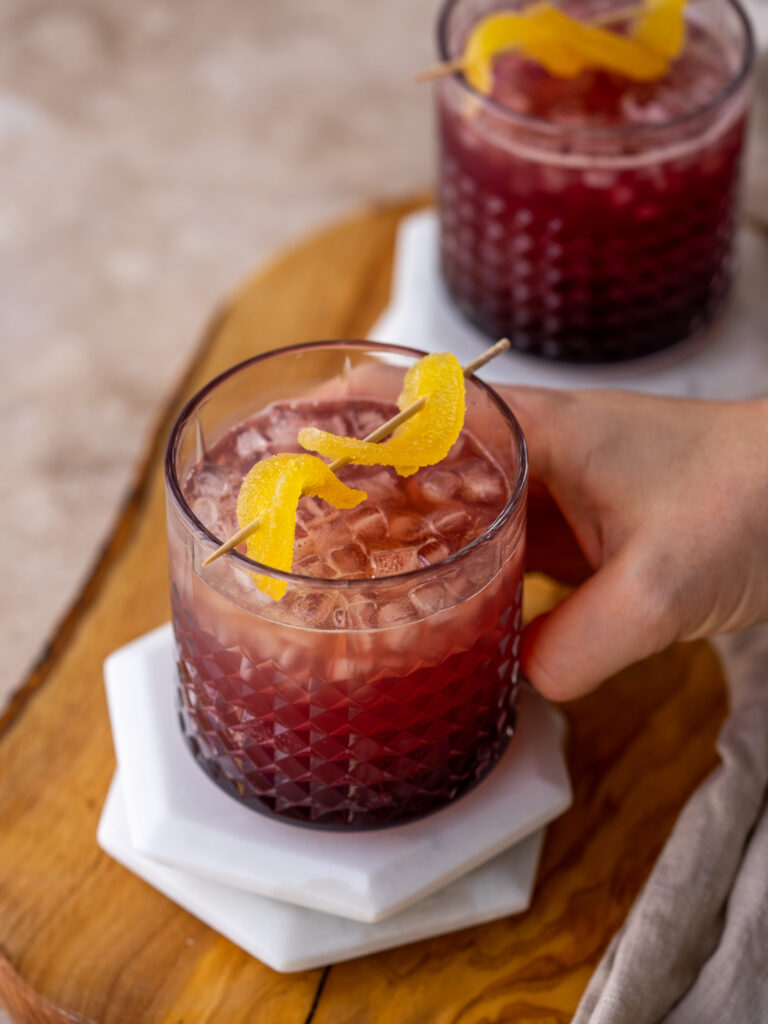 three quarter view of a hand grabbing a cranberry moscow mule in a glass