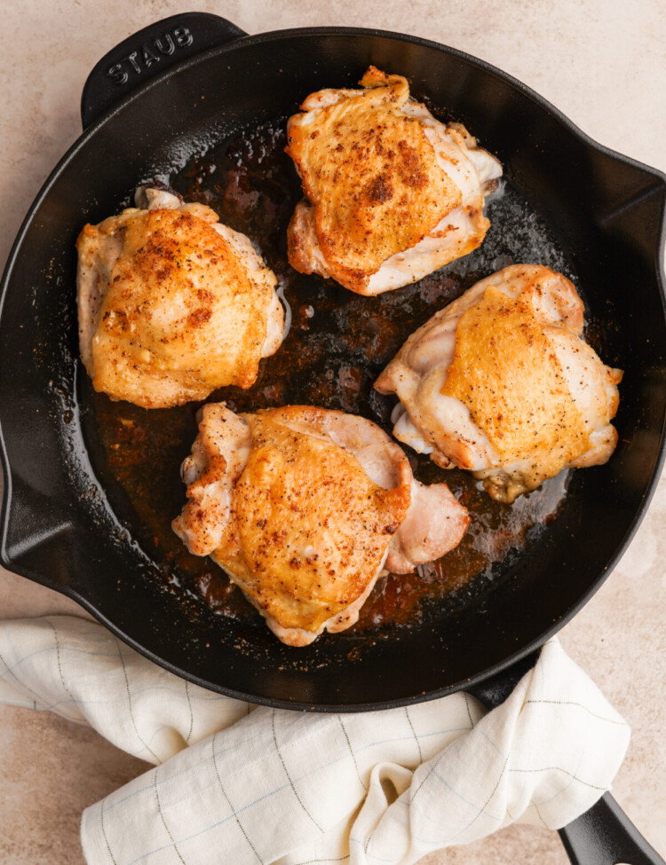 Above view of four bone in skin on chicken thighs in a cast iron skillet with a dish towel around the handle of the skillet